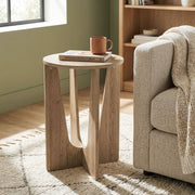 Round side table beside a cream sofa in a green room with a mug and book on top