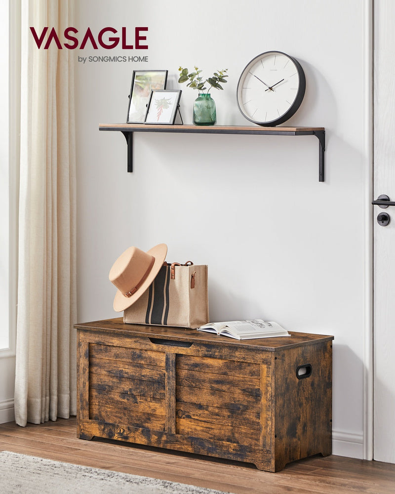 Closed rustic brown storage chest used as an entryway bench below a wall shelf with a hat and bag on top