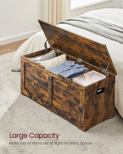 Rustic brown storage chest open in a bedroom holding a pillow, folded clothes and a book