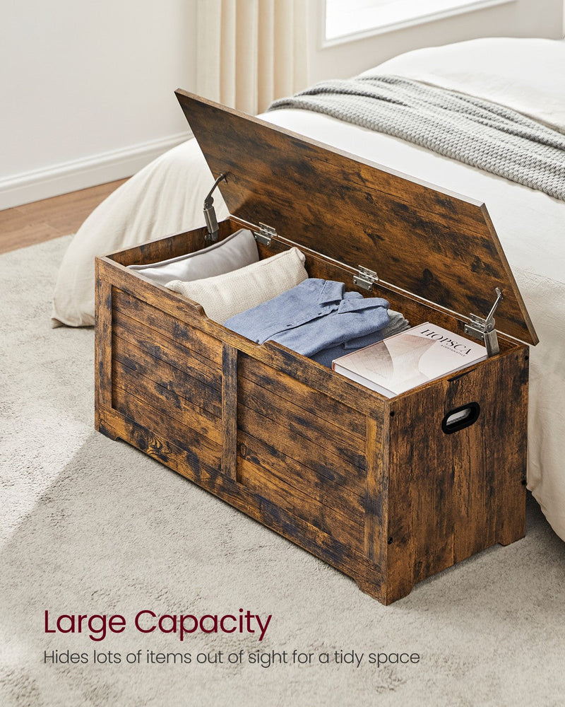 Rustic brown storage chest open in a bedroom holding a pillow, folded clothes and a book