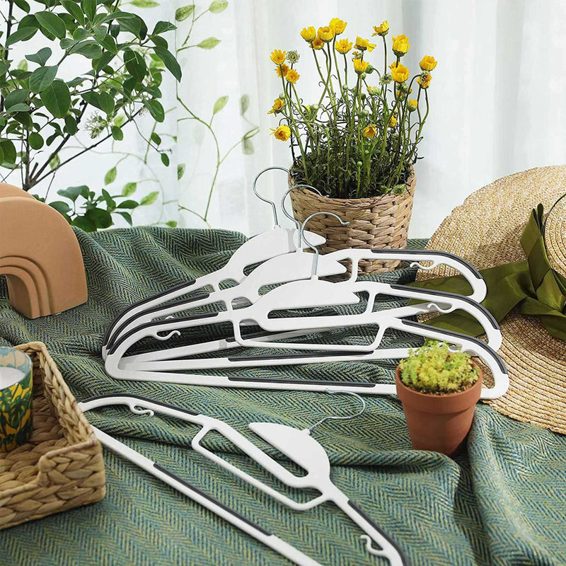 White S-shaped neck coat hangers laid on a green cloth beside a straw hat and potted plants