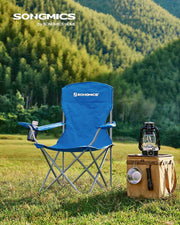 Single blue camping chair set up on grass beside a lantern and cool box with green hills behind
