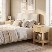 Oak bedside table beside a bed with books on the open lower shelf