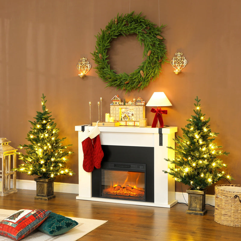 Two lit trees in pots either side of a white fireplace under a wreath