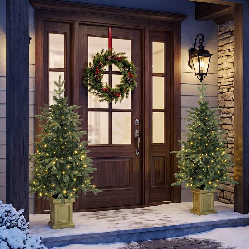 Two lit Aspen Fir trees either side of a dark wooden front door with a wreath
