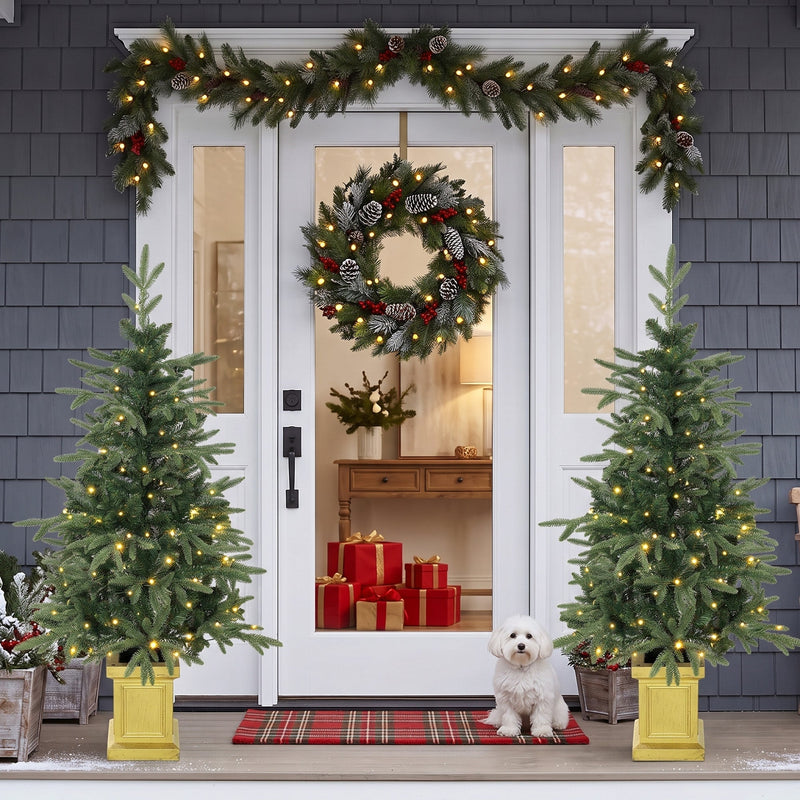 Two lit Aspen Fir trees beside a white front door with a garland and small dog