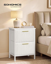 One white corduroy bedside table styled with a table lamp, clock and mug beside an upholstered bed
