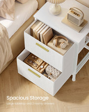 Overhead view of both white bedside table drawers open, holding books, headphones, glasses and jewellery