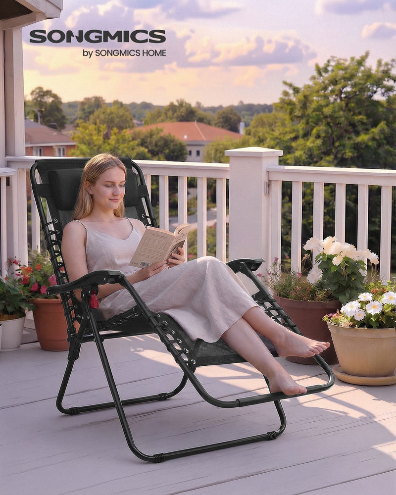 Woman reading a book while reclining in a black zero gravity chair on a sunny balcony