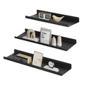 Three black metal wall shelves staggered on a white background with books, a clock and frames