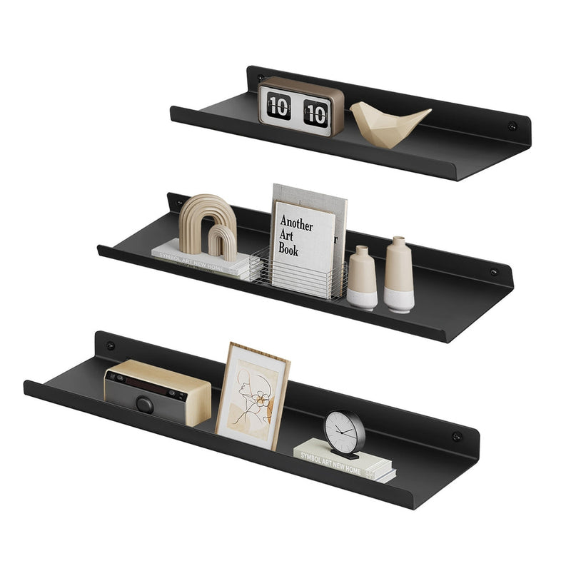 Three black metal wall shelves staggered on a white background with books, a clock and frames