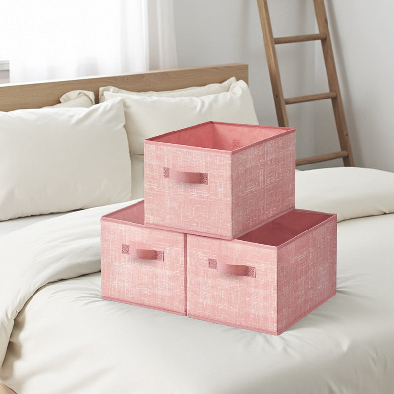 Three pink fabric storage boxes stacked on a white duvet in a bright bedroom