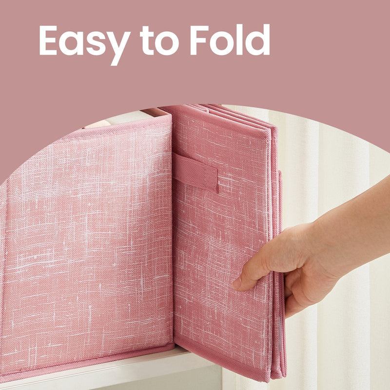 Hand folding a pink fabric storage box flat to show how it collapses for storage