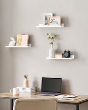 White picture ledge shelves above a home office desk holding frames and a plant