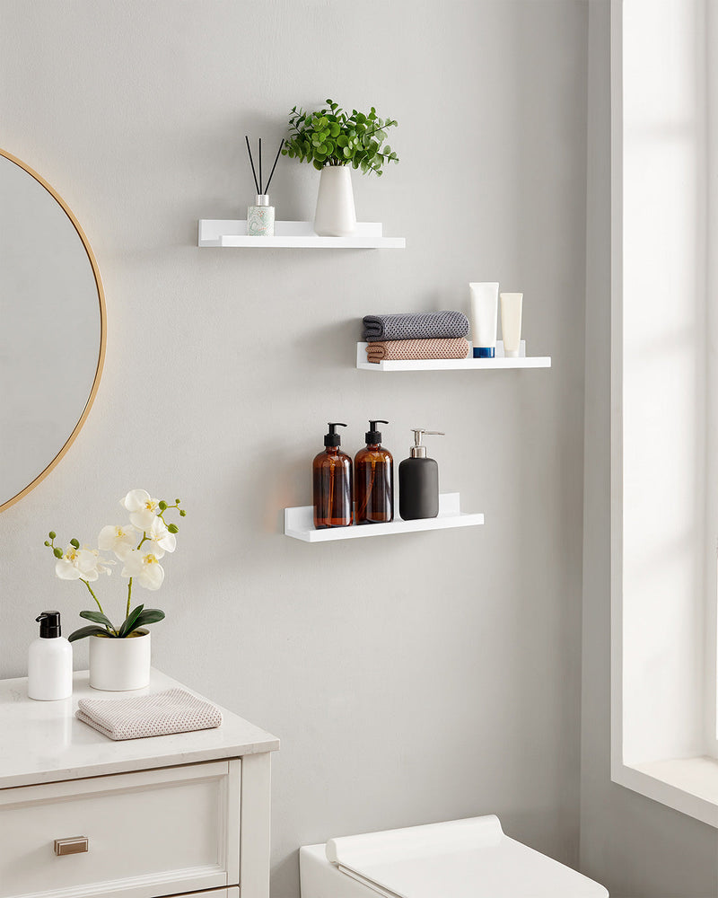 Three white ledge shelves in a bathroom holding toiletries, towels and flowers