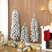 Three flocked pencil trees in front of a fireplace with wrapped gifts
