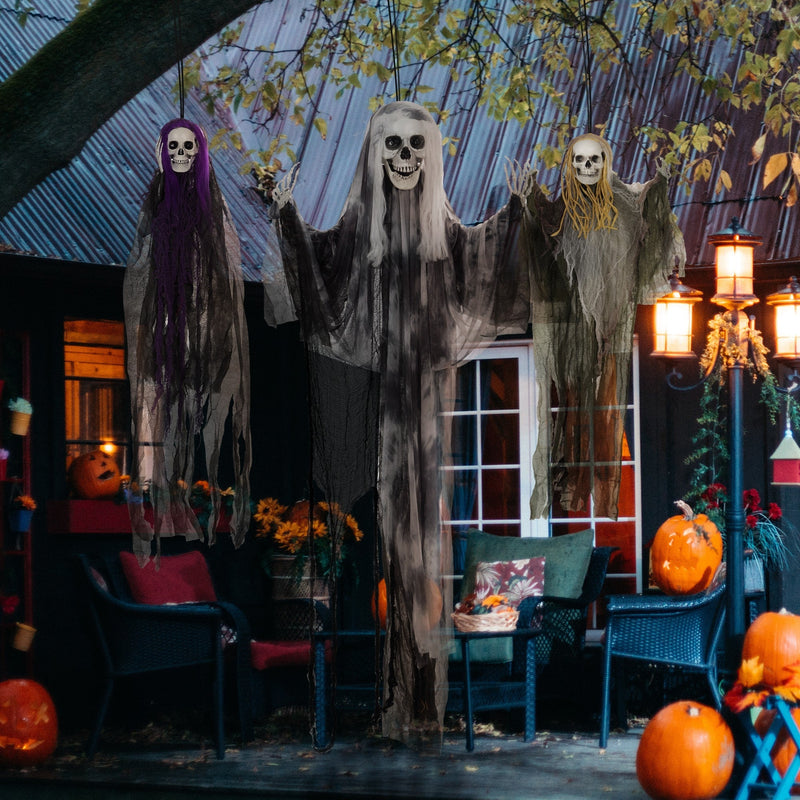 Three hanging skeleton decorations displayed on a porch at night with pumpkins