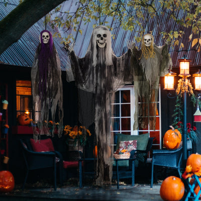 Three hanging skeleton decorations displayed on a porch at night with pumpkins