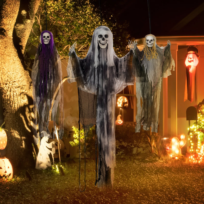 Three hanging skeleton decorations hung outside a house among garden lights
