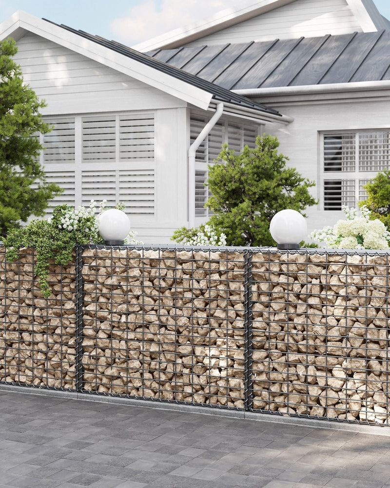 Long stone gabion boundary wall in front of a white house with globe lights on top