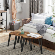 Nesting tables grouped beside a bed on a striped rug with a plant and magazines