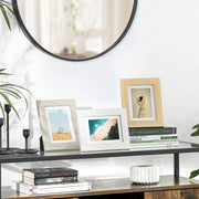 Three of the photo frames standing on a black console table below a round mirror, beside books and candles