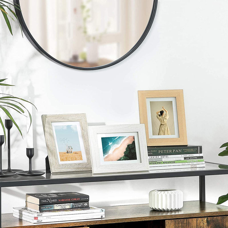 Three of the photo frames standing on a black console table below a round mirror, beside books and candles