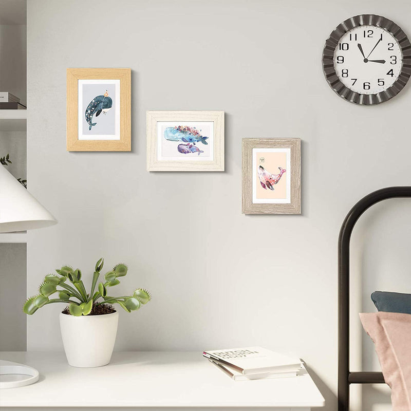 The three frames hung in a staggered line on a white bedroom wall near a shelf and a wall clock