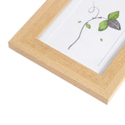 Angled close-up of the light wood grain frame corner and the white photo mount behind the glass