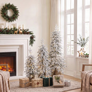 Three flocked Christmas trees beside a white fireplace with candles and wrapped gifts