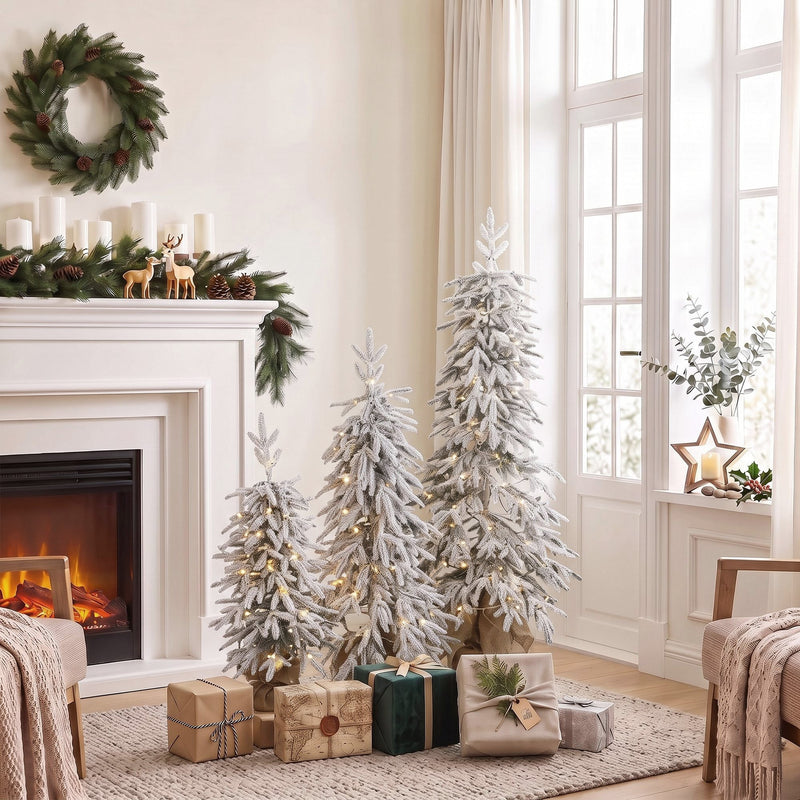 Three flocked Christmas trees beside a white fireplace with candles and wrapped gifts