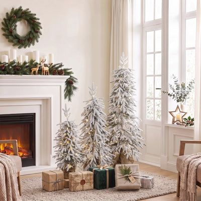 Three flocked Christmas trees beside a white fireplace with candles and wrapped gifts