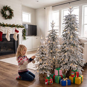 Child hanging a bauble on the lit flocked trees by a fireplace with stockings