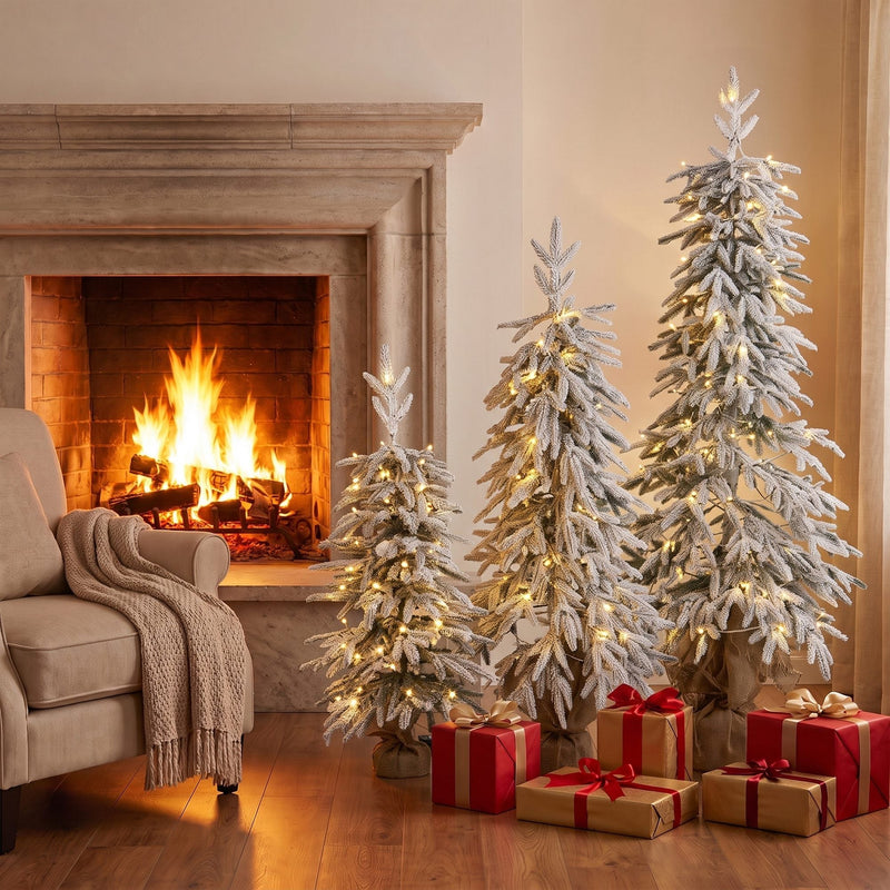 Three lit flocked trees by a stone fireplace with red gift boxes
