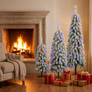 Three lit flocked trees with multicolour lights by a stone fireplace