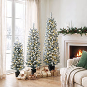 Three flocked Christmas trees with warm white lights by a window and fireplace with wrapped gifts