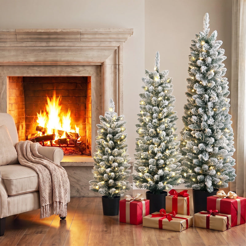 Three lit flocked Christmas trees by a stone fireplace with red gift boxes