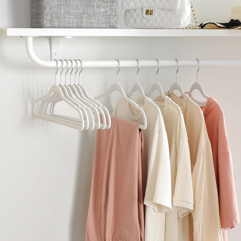 Row of white velvet hangers holding jumpers and tops under a wall shelf