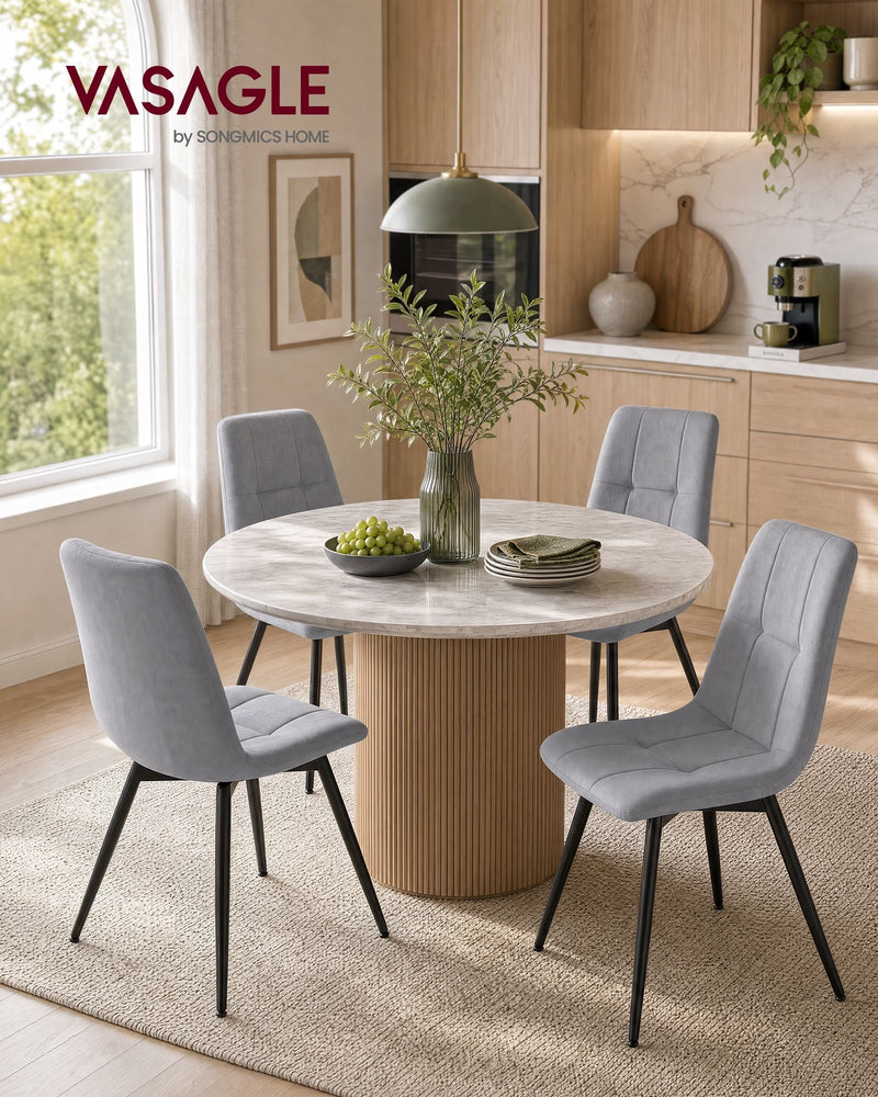 Four grey velvet dining chairs around a round table in a bright kitchen