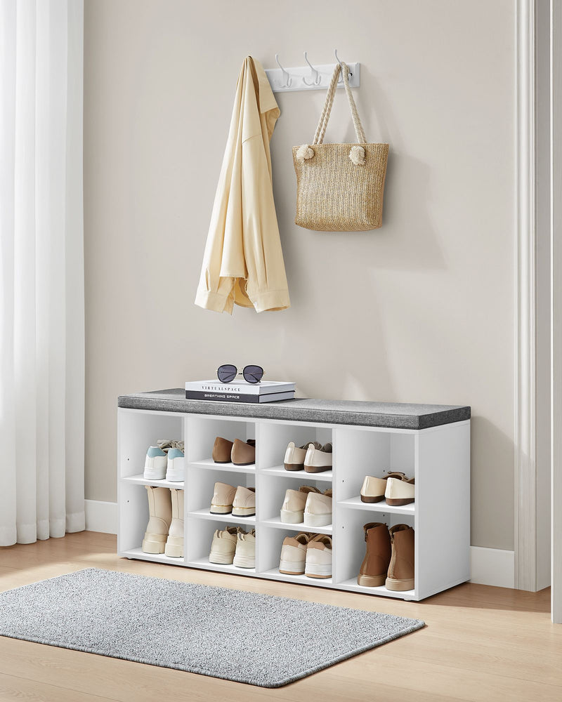 White shoe bench in a hallway below a coat rack with a jacket and straw basket bag