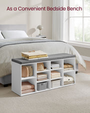 White shoe bench used at the end of a bed holding folded clothes, books and baskets