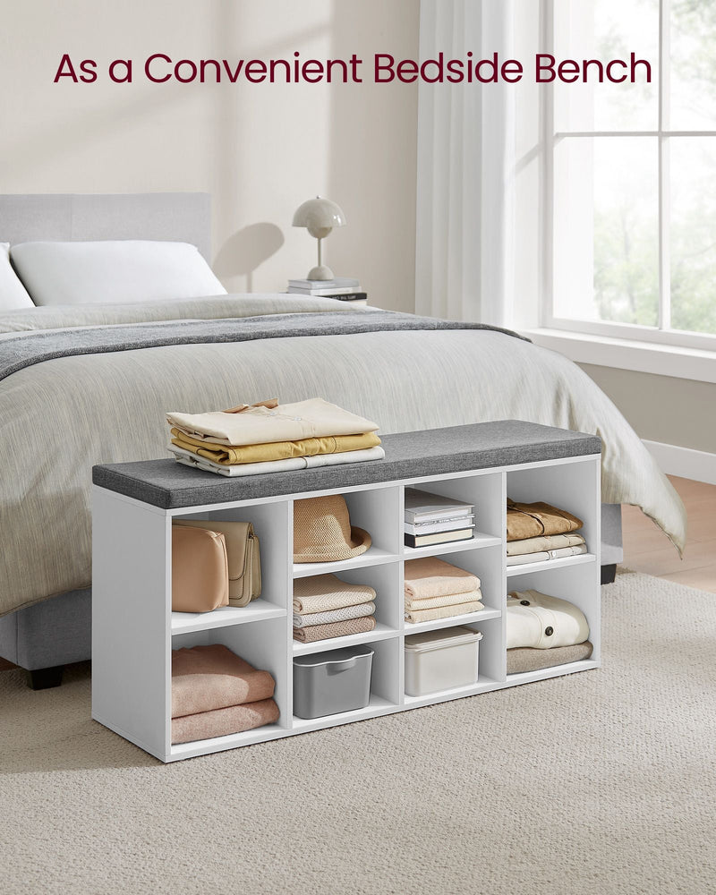 White shoe bench used at the end of a bed holding folded clothes, books and baskets