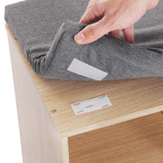 Hand lifting the grey seat cushion off the natural wood bench top to show the fastening