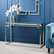 Glass and silver console table in an entryway beneath a round mirror