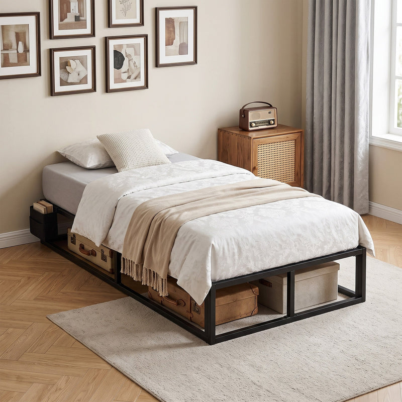 Single bed frame with white bedding in a bedroom, with a vintage suitcase and storage box under the frame
