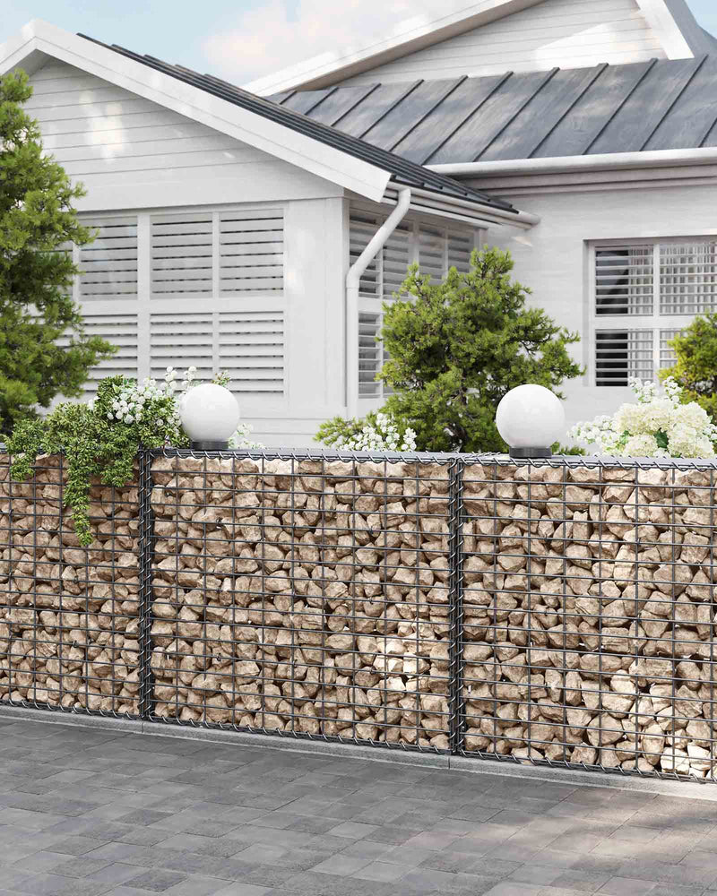 Stone gabion base running along a white house wall beside a downpipe