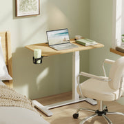 The table used beside a bed and a cream armchair, holding a laptop, books and a cup in the side holder