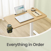 Overhead view of the tabletop with a tablet propped in the device slot, a closed laptop, coffee and a notepad