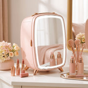 Pink mini fridge on a dressing table beside flowers, lipsticks and makeup brushes