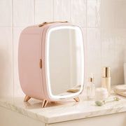 Pink fridge with its lit mirror closed on a marble surface beside serum and cream